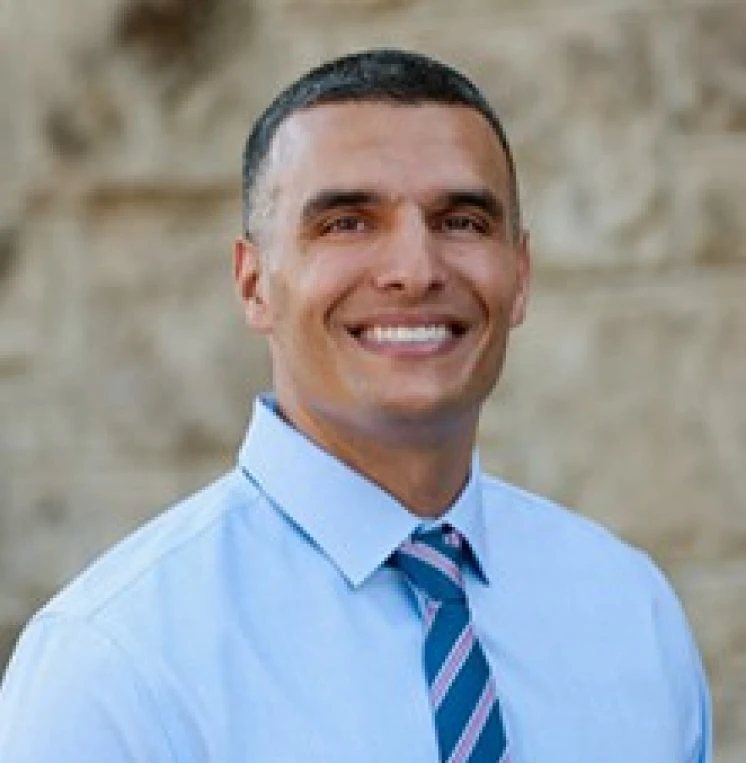 Smiling cosmetic and family dentist headshot in blue shirt and striped tie outdoors.